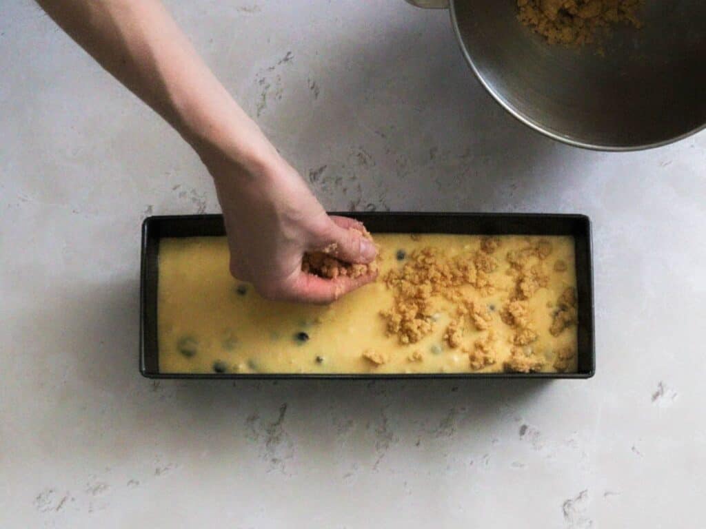 Adding the crumble topping to sourdough blueberry bread.