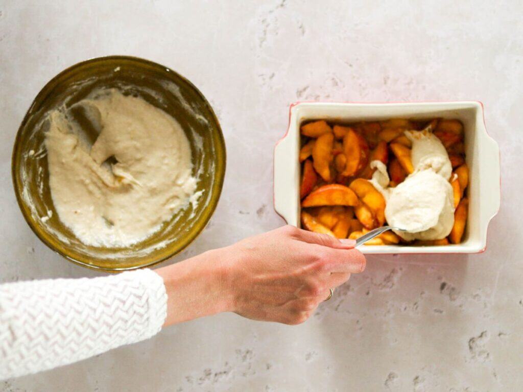 Scooping the batter on top of the sourdough peach cobbler.