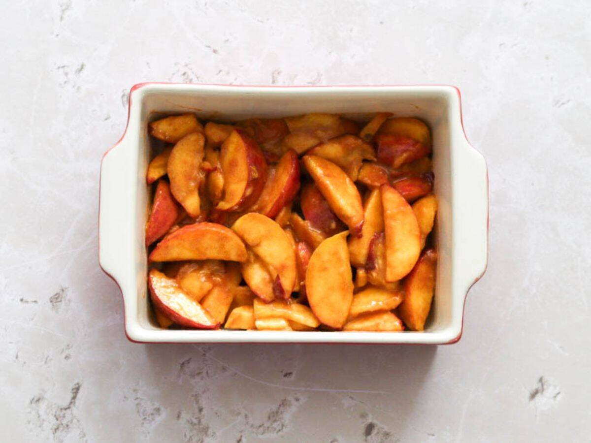 Sliced peaches for sourdough cobbler in a white oven dish.
