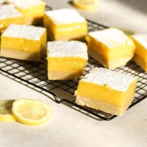 Five sourdough lemon bars on a cooling rack with lemons