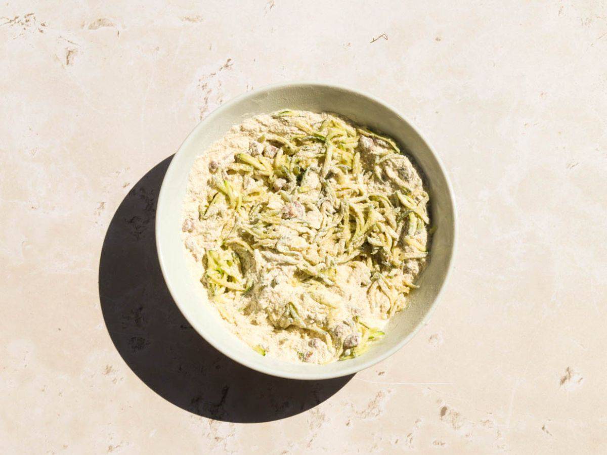 Mixing the dry ingredients for discard zucchini muffins in a yellow bowl.