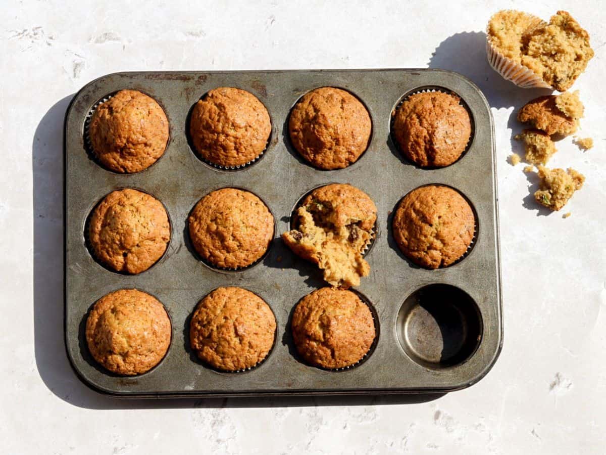Sourdough zucchini muffins in a muffin tin with one muffin in half to see the texture.