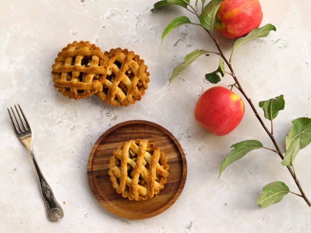 Three miniature apple pies, a fork, and apples.