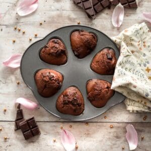 Sourdough chocolate muffins in a muffin tin with a towel.
