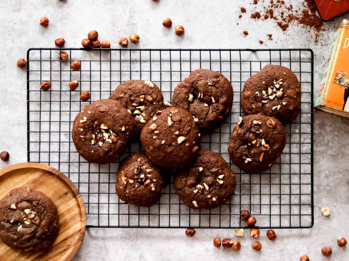 Sourdough chocolate cookies on a wire rack with hazelnuts and cocoa powder.