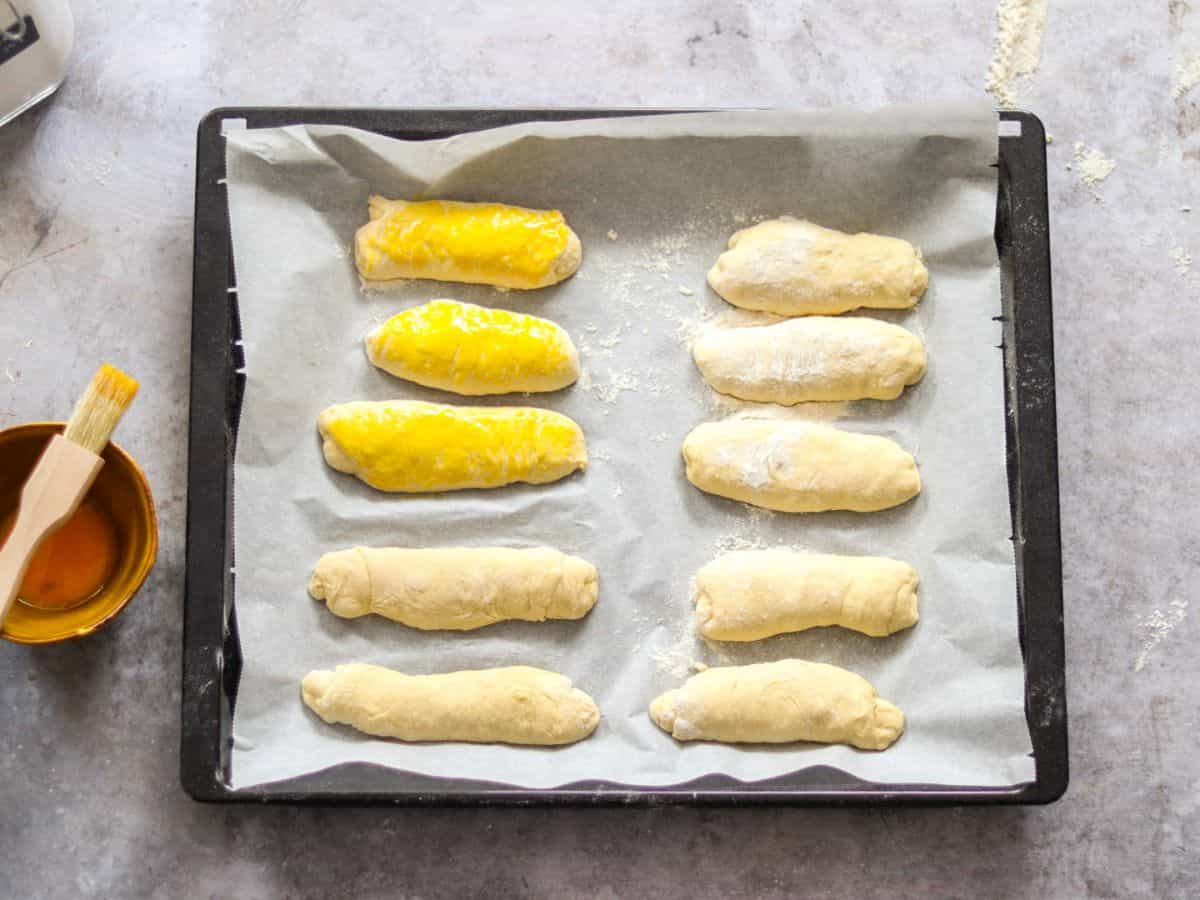 Unbaked sourdough hot dog buns on a baking tray.